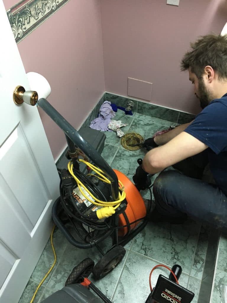 Plumber on his knee in front of toilet bowl and pushing a camera into toilet hole to look into the clogged drain in a basement and to find out where the sanitary drain is clogged