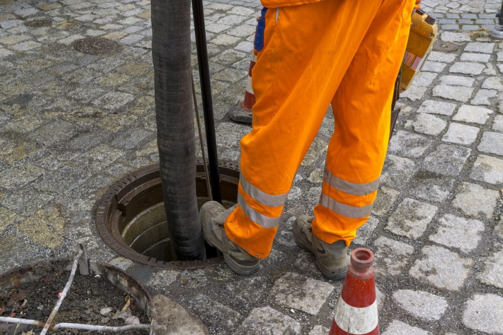 Expert plumbers using special tools to attend to a city's clogged area drain.