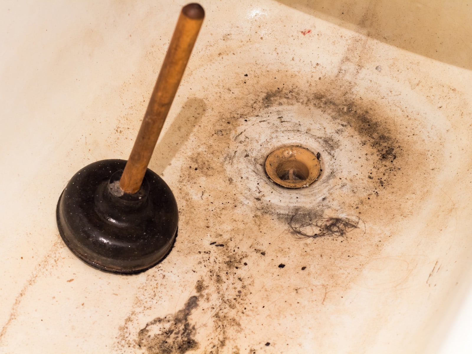 A clogged and dirty bathtub with a drain plunger.
