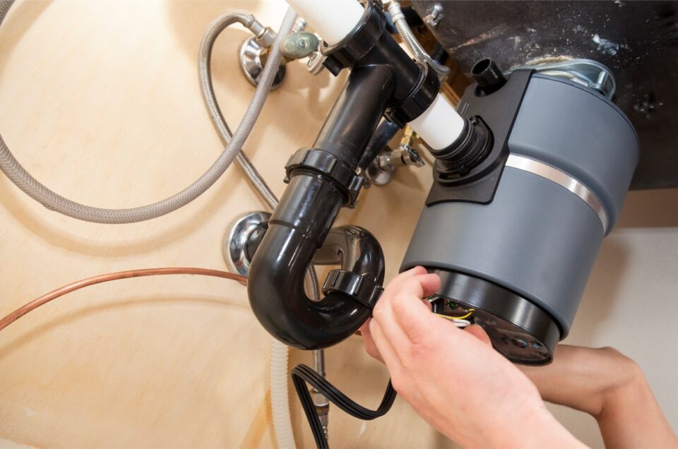 Cleaning a garbage disposal - A person's hand checking a kitchen garbage disposal located under the sink.