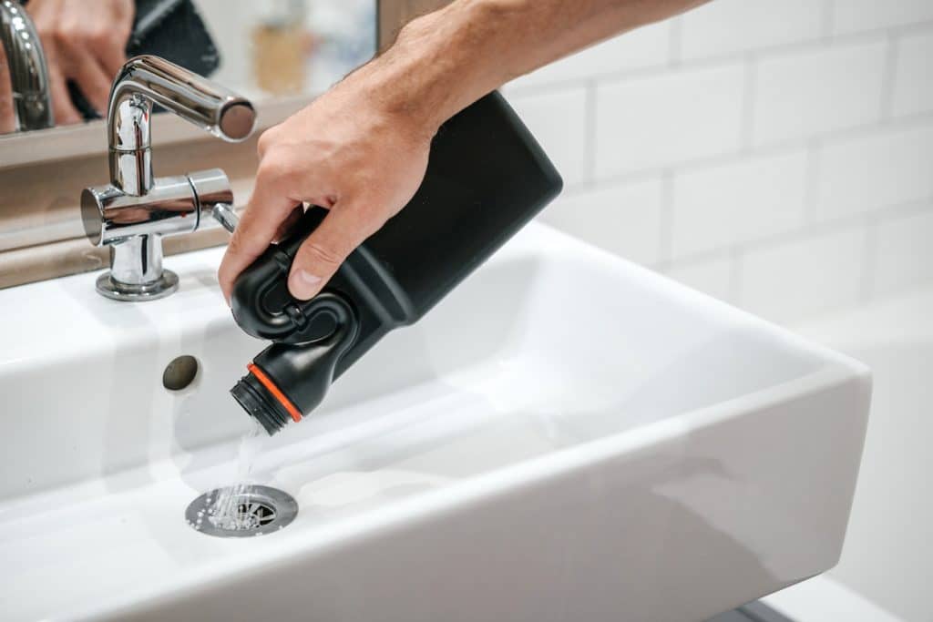 Person's hand pouring root killer for sewer lines down a drain.