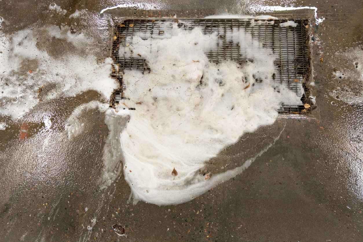 Cleaning a clogged garage drain - Clogged floor grate with dirty soap suds and dried leaves.