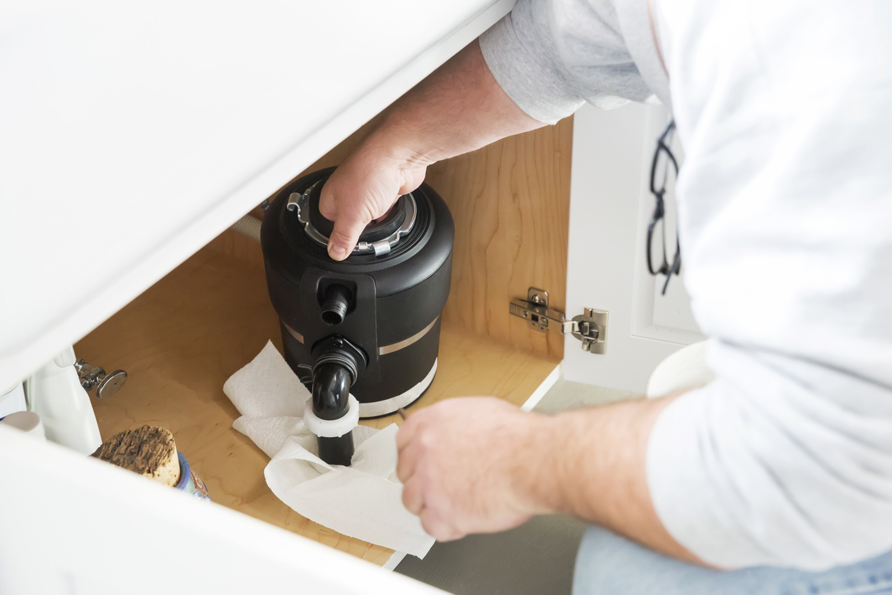 Cleaning a garbage disposal - A man cleaning a kitchen garbage disposal using paper towels.