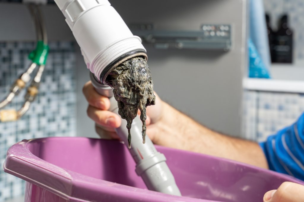 Plumber removing a large hair blockage from a bathroom pipe - causes of slow-draining sinks.