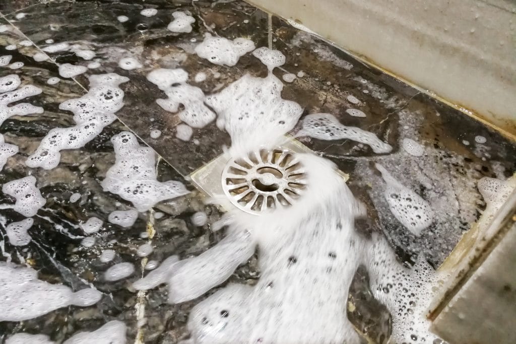 Soap foam suds and water flowing into bathroom drainage hole after being snaked from a shower drain clog