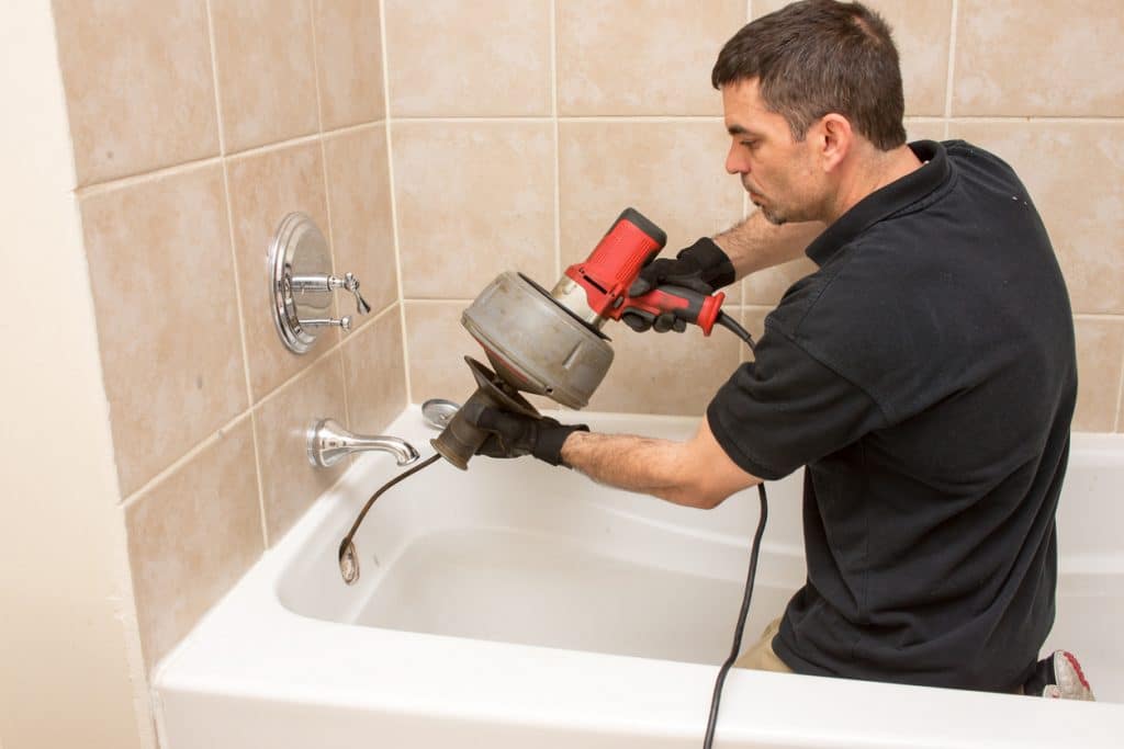 Plumber snaking shower drain with an electric auger.