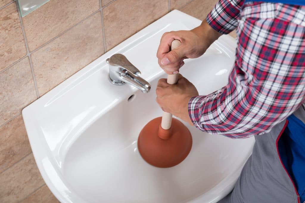 A man using a plunger to unclog his bathroom sink drain at home.