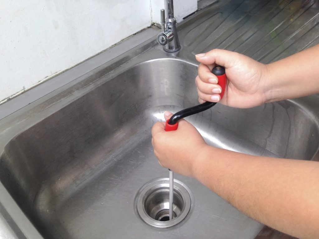 Woman unclogging her kitchen drain using a flexible spring drain cleaner.