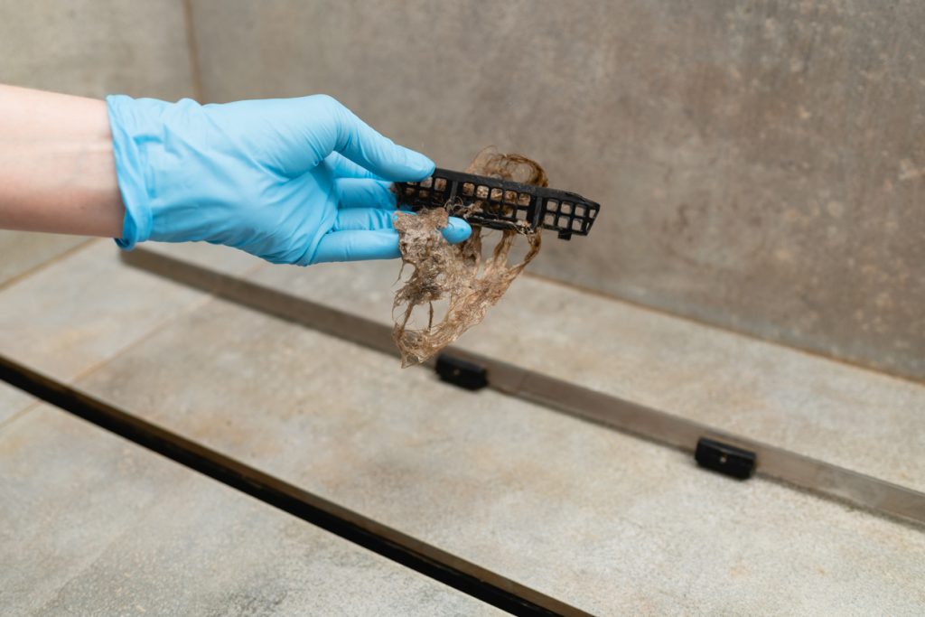 Preventing drain clogs - Person wearing a glove while holding a bathroom hair catcher.