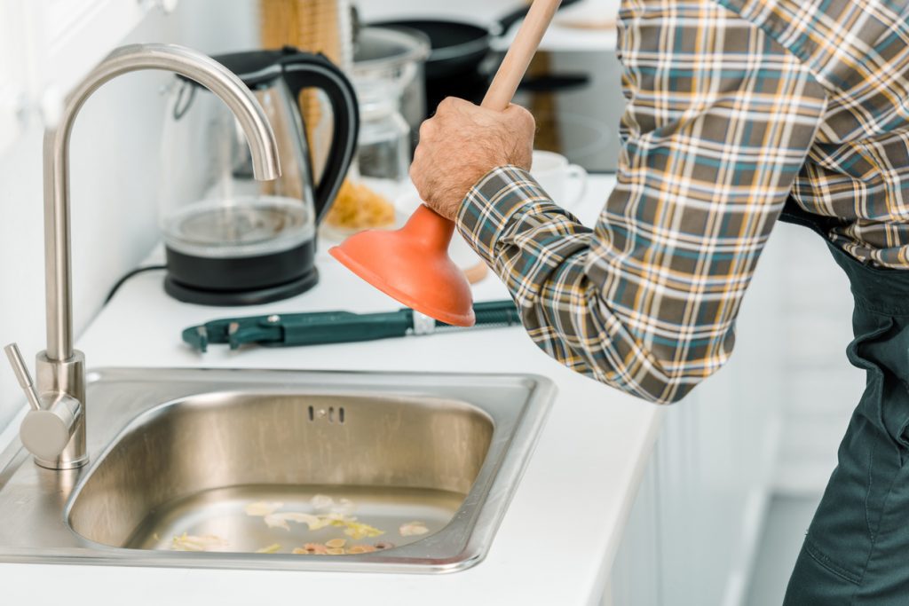 Man using a sink plunger to unclog blockages in a kitchen sink - solutions for slow-draining sinks.